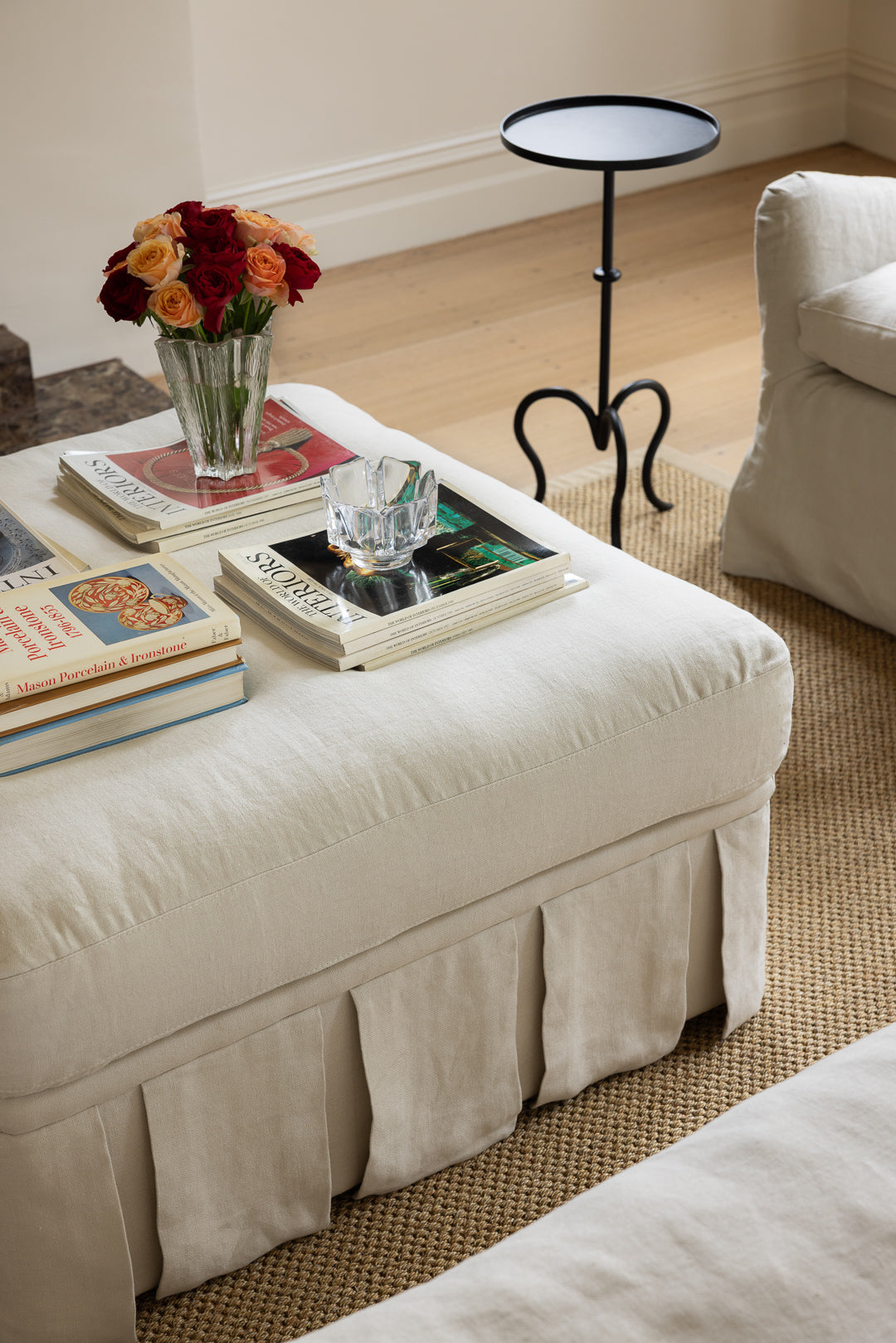Rachel Donath Nora ottoman large in creme with books, a vase of flowers, and a small table in a living room setting.